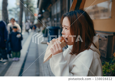 一位二十多歲的女子一邊在旅遊景點漫步,一邊享用新鮮出爐的麵包。 一位二十多歲的女子一邊在旅遊景點漫步,一邊享用新鮮出爐的麵包。 138016812