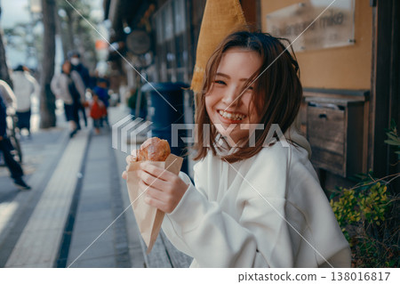 A woman in her 20s enjoying freshly baked bread while strolling around a tourist spot. A woman in her 20s enjoying freshly baked bread while strolling around a tourist spot. 138016817
