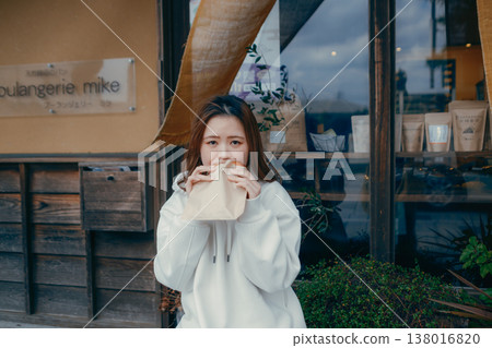 一位二十多歲的女子一邊在旅遊景點漫步,一邊享用新鮮出爐的麵包。 一位二十多歲的女子一邊在旅遊景點漫步,一邊享用新鮮出爐的麵包。 138016820