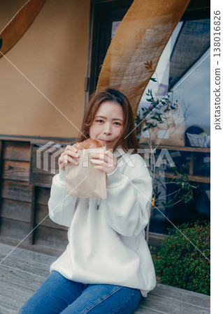 一位二十多歲的女子一邊在旅遊景點漫步，一邊享用新鮮出爐的麵包。 138016826