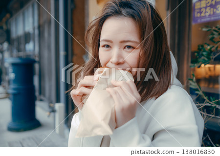 A woman in her 20s enjoying freshly baked bread while strolling around a tourist spot. A woman in her 20s enjoying freshly baked bread while strolling around a tourist spot. 138016830