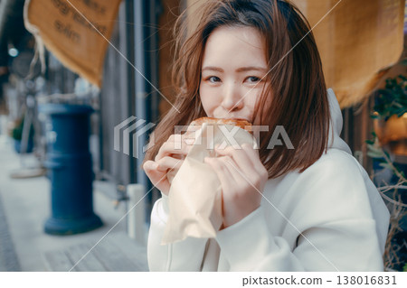 一位二十多歲的女子一邊在旅遊景點漫步，一邊享用新鮮出爐的麵包。 138016831