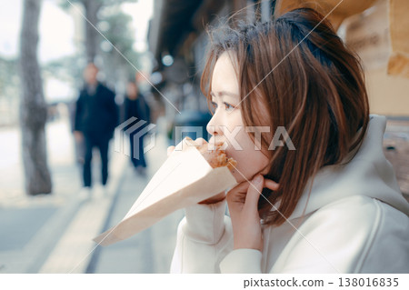 一位二十多歲的女子一邊在旅遊景點漫步,一邊享用新鮮出爐的麵包。 一位二十多歲的女子一邊在旅遊景點漫步,一邊享用新鮮出爐的麵包。 138016835
