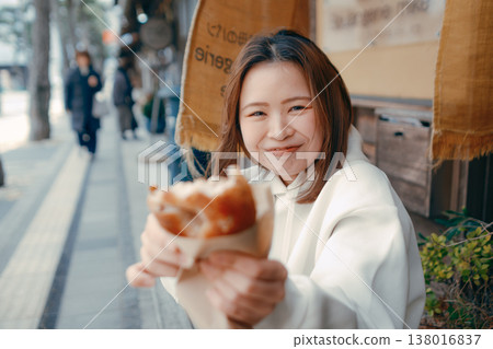 一位二十多歲的女子一邊在旅遊景點漫步,一邊享用新鮮出爐的麵包。 一位二十多歲的女子一邊在旅遊景點漫步,一邊享用新鮮出爐的麵包。 138016837
