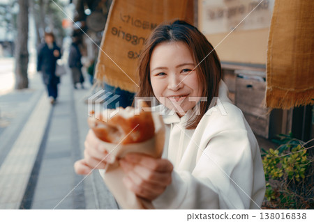 一位二十多歲的女子一邊在旅遊景點漫步,一邊享用新鮮出爐的麵包。 一位二十多歲的女子一邊在旅遊景點漫步,一邊享用新鮮出爐的麵包。 138016838