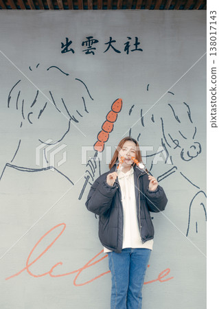 一位二十多歲的微笑的女子在旅遊景點吃草莓糖。 一位二十多歲的微笑的女子在旅遊景點吃草莓糖。 138017143