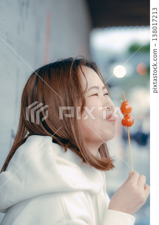 一位二十多歲的女性在旅遊景點享用草莓糖的肖像。 一位二十多歲的女性在旅遊景點享用草莓糖的肖像。 138017213