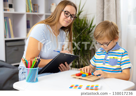 Woman Observing Young Boy Solving Puzzle at Table in Bright Room Woman Observing Young Boy Solving Puzzle at Table in Bright Room 138017236