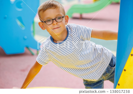 Young boy with glasses playing at colorful outdoor playground Young boy with glasses playing at colorful outdoor playground 138017238