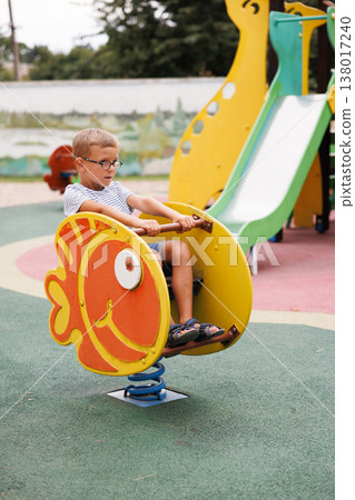 Young boy playing on fish-shaped spring rocker at playground Young boy playing on fish-shaped spring rocker at playground 138017240