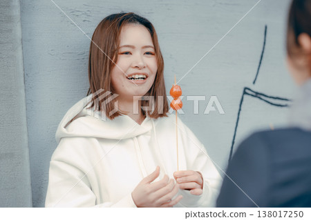 A woman in her 20s enjoying strawberry candy with a friend at a tourist spot. 138017250