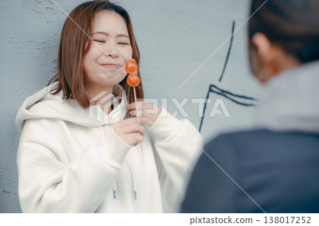 A woman in her 20s enjoying strawberry candy with a friend at a tourist spot. 138017252