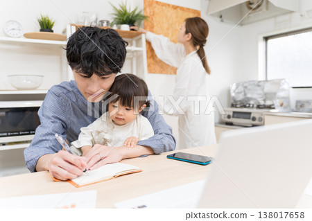 A young father takes notes and works while taking care of his child in the dining room: A scene of working from home while raising a child. 138017658