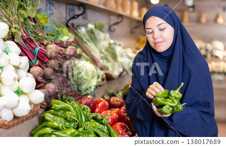 Young european woman in muslim abaya and chador choosing peppers in store Young european woman in muslim abaya and chador choosing peppers in store 138017689