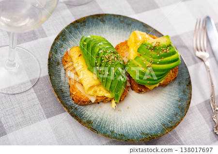 Hearty sandwich with toast, cheese, plate of egg omelet and pieces of avocado. Hearty sandwich with toast, cheese, plate of egg omelet and pieces of avocado. 138017697