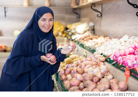 Young european girl in muslim abaya and chador choosing onions at market Young european girl in muslim abaya and chador choosing onions at market 138017752