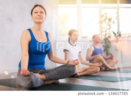 Middle-aged woman, man, preteen girl and boy practicing Padmasana with crossed legs on mats during family Hatha yoga class in wellness studio Middle-aged woman, man, preteen girl and boy practicing Padmasana with crossed legs on mats during family Hatha yoga class in wellness studio 138017785