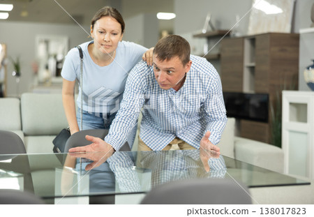 Positive couple, woman and man talking friendly while choosing new dining table for apartment in furniture store 138017823