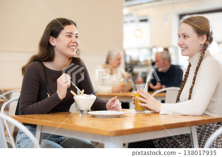 Two positive girls chatting over juice and eat ice cream while sitting at small table in cafe Two positive girls chatting over juice and eat ice cream while sitting at small table in cafe 138017935