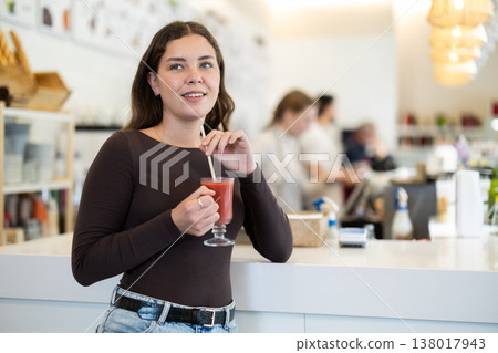 Young woman drinks tomato juice at table in cafe 138017943