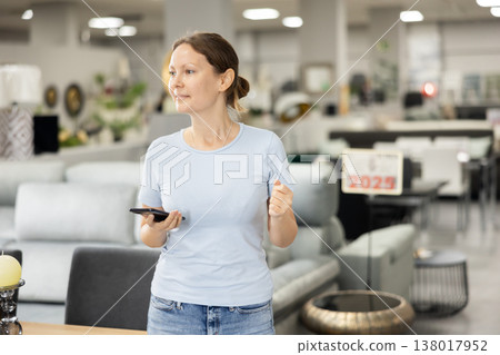 Portrait of woman consulted on phone while looking for new furniture in salon 138017952
