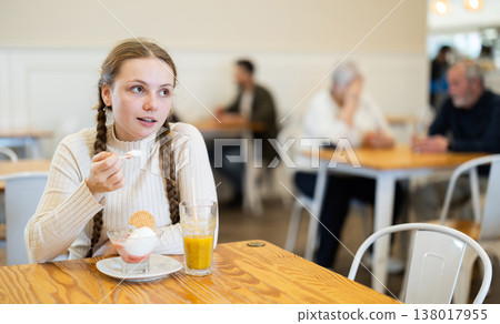 Food court teen girl visitor sits near table, eating ice cream in chain cafe shop Food court teen girl visitor sits near table, eating ice cream in chain cafe shop 138017955