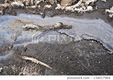 Oil slick creating iridescent rainbow colors spreading across water puddle and melting snow on cracked asphalt street Oil slick creating iridescent rainbow colors spreading across water puddle and melting snow on cracked asphalt street 138017968