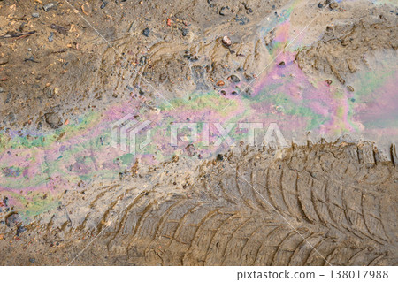 Ground showing an iridescent oil spill polluting dirty puddle with car tire tracks. A symbol of environmental contamination Ground showing an iridescent oil spill polluting dirty puddle with car tire tracks. A symbol of environmental contamination 138017988