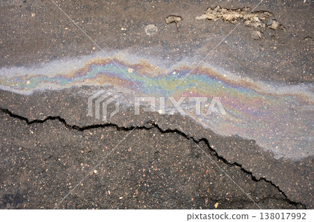 Iridescent oil slick spreading on damaged asphalt surface, reflecting vibrant rainbow colors, highlighting an environmental pollution issue Iridescent oil slick spreading on damaged asphalt surface, reflecting vibrant rainbow colors, highlighting an environmental pollution issue 138017992