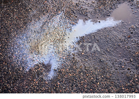 Iridescent oil slick spreading in a puddle on wet asphalt, showing environmental pollution and chemical waste 138017993