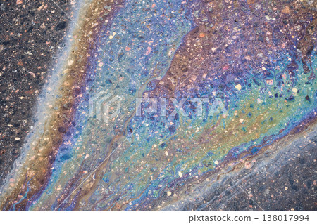 Gasoline spill on dark wet pavement displaying colorful iridescent film and abstract fluid patterns, symbolizing environmental impact 138017994
