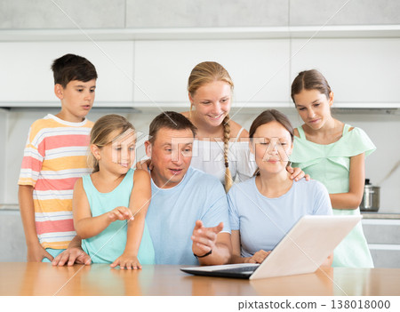 Large family is sitting in kitchen next to laptop and making video call to grandparents 138018000