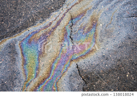 Iridescent oil spill on asphalt, showing environmental petroleum pollution and fluid rainbow color texture 138018024