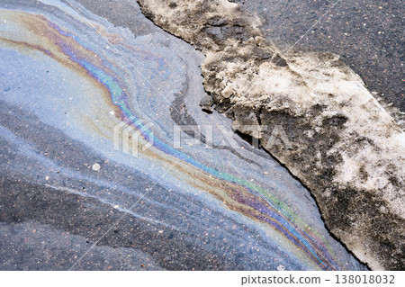 Glistening oil slick displaying vivid colors on the damp pavement, depicting the consequences of pollution, environmental harm, and intricate abstract designs 138018032