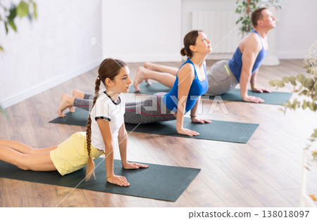 Friendly sporty parents with tween daughter and son performing Cobra Pose or Bhujangasana on gymnastic mats barefoot in yoga studio. Family health concept 138018097