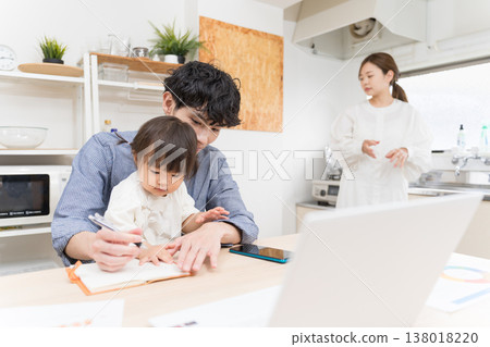A young father takes care of his child while working from home in the dining room. 138018220