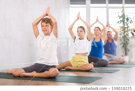 Happy preteen boy practicing half lotus pose of yoga with his family Happy preteen boy practicing half lotus pose of yoga with his family 138018225