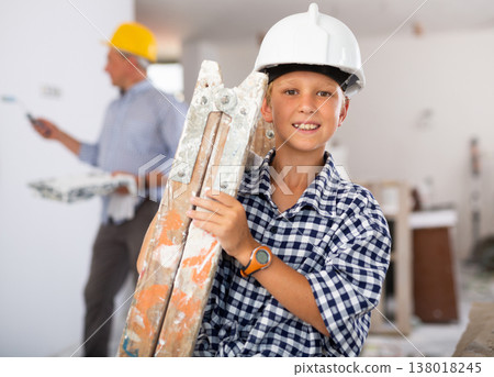 Portrait of positive boy carrying stepladder in construction site Portrait of positive boy carrying stepladder in construction site 138018245