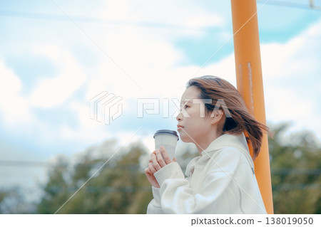 一位二十多歲的女性在旅遊景點悠閒地享用咖啡，畫面輕鬆愜意。 138019050