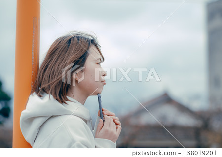 一位二十多歲的女性在旅遊景點看著她的智慧型手機的側面肖像。 138019201