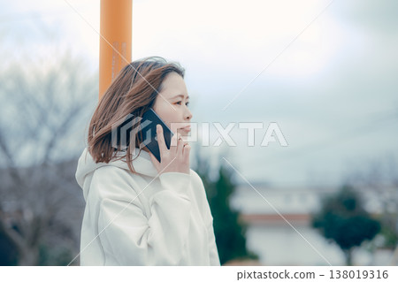 A profile portrait of a woman in her 20s talking on the phone outdoors. 138019316