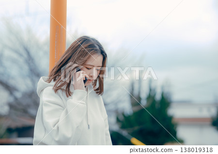 A profile portrait of a woman in her 20s talking on the phone outdoors. A profile portrait of a woman in her 20s talking on the phone outdoors. 138019318