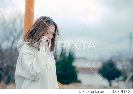 A profile portrait of a woman in her 20s talking on the phone outdoors. 138019320