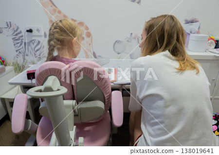 Parent guiding child at study chair, mother leans over pink ergonomic seat while child works on paper, animal-print wallpaper and tidy desk area, calm nurturing atmosphere with collaborative focus Parent guiding child at study chair, mother leans over pink ergonomic seat while child works on paper, animal-print wallpaper and tidy desk area, calm nurturing atmosphere with collaborative focus 138019641