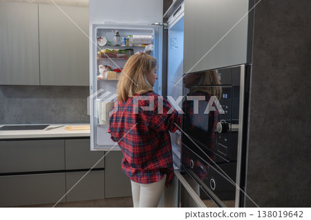 Woman checking refrigerator near oven, home chef prepping dinner, scanning labels and arranging ingredients, stainless countertop and builtin oven, focused expression, minimalist kitchen design, Woman checking refrigerator near oven, home chef prepping dinner, scanning labels and arranging ingredients, stainless countertop and builtin oven, focused expression, minimalist kitchen design, 138019642