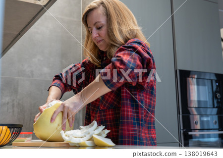 Woman peeling pomelo on countertop in modern kitchen wearing red plaid shirt removing pith and peel arranging juicy segments on board focused home cook preparing healthy snack soft daylight stainless Woman peeling pomelo on countertop in modern kitchen wearing red plaid shirt removing pith and peel arranging juicy segments on board focused home cook preparing healthy snack soft daylight stainless 138019643