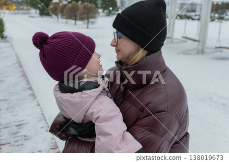 young mother holding daughter close on snowy sidewalk, maroon puffer jacket and black beanie, daughter in pink coat with pompom beanie, gentle eye contact and warm embrace, visible breath in cold air, young mother holding daughter close on snowy sidewalk, maroon puffer jacket and black beanie, daughter in pink coat with pompom beanie, gentle eye contact and warm embrace, visible breath in cold air, 138019673
