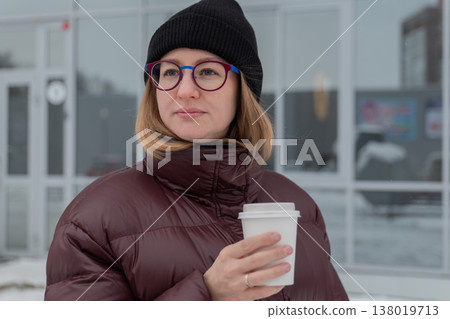 Woman sipping coffee outside storefront, casual streetstyle portrait with confident expression, maroon puffer coat and black beanie, round glasses catching soft light, neutral winter tones, subtle Woman sipping coffee outside storefront, casual streetstyle portrait with confident expression, maroon puffer coat and black beanie, round glasses catching soft light, neutral winter tones, subtle 138019713