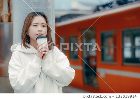 Portrait of a woman in her 20s holding a coffee on a train platform. 138019914