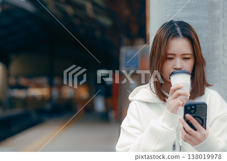 一位二十多歲的女性手捧咖啡站在火車站台上的肖像。 138019978